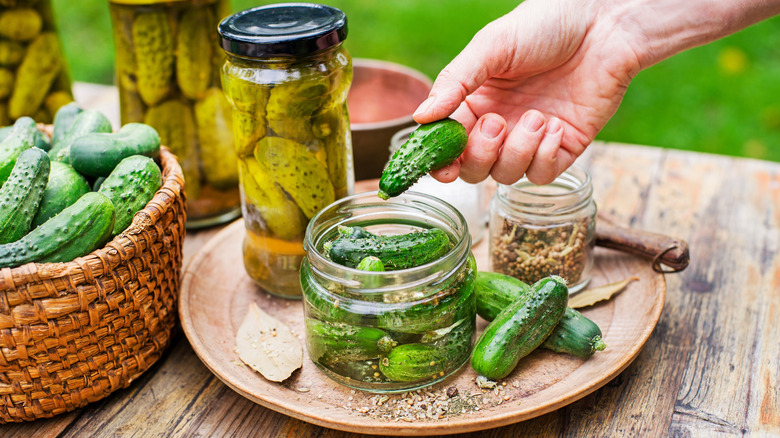 Jars and a basket of pickles on a wooden table outside