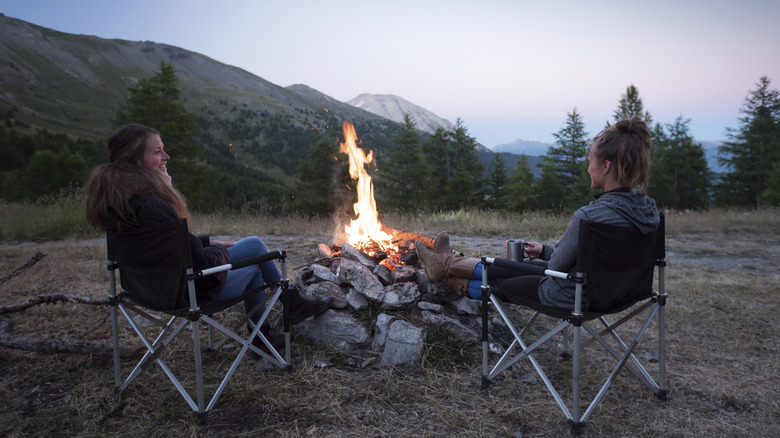 Two women sitting by a campfire at dusk