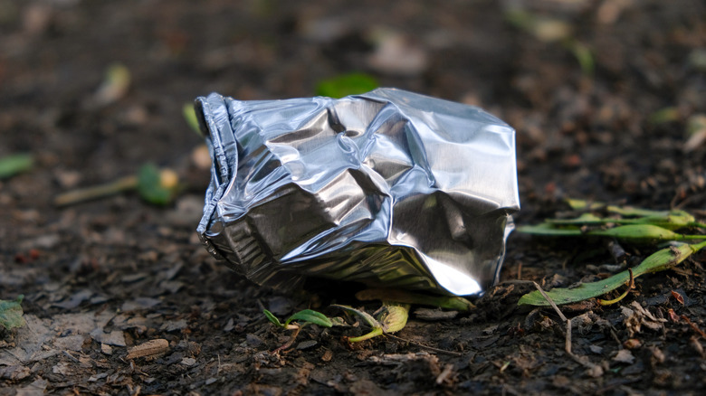 A piece of aluminum foil reflecting the sun outside in the dirt.