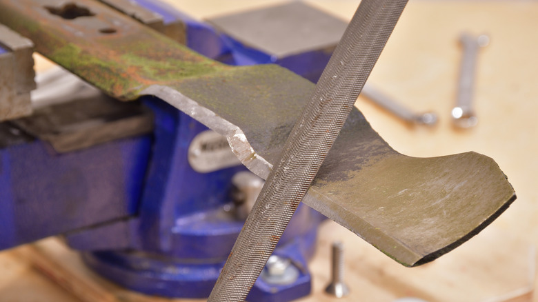 Filing a mower blade on a vice