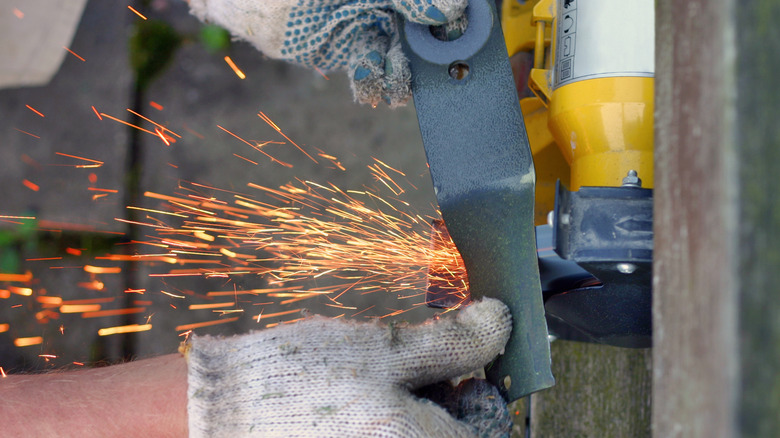 Person using bench grinder to sharpen mower blade