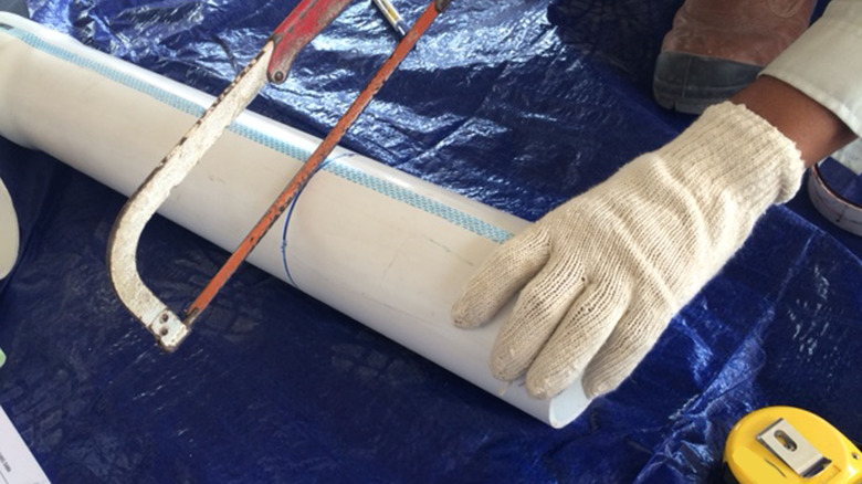 A person cutting a pvc pipe with a saw