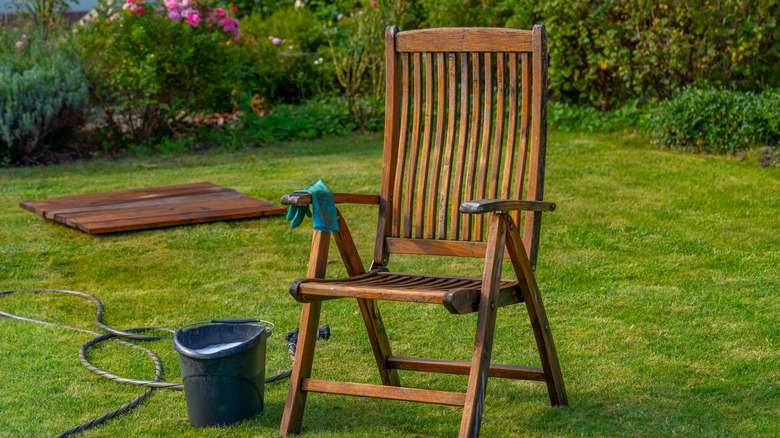 A wooden garden chair next to a cleaning bucket and hose