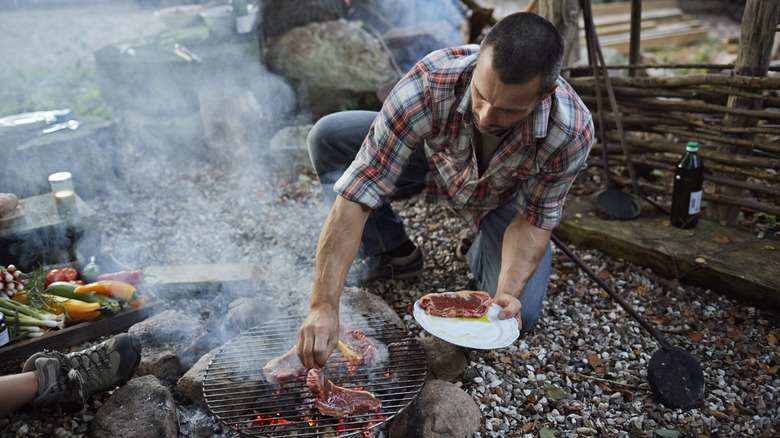 Camper adding steak to a grill over a fire
