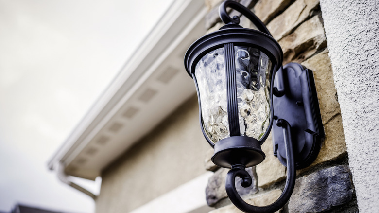 A weatherproof light fixture hangs on the exterior of a house