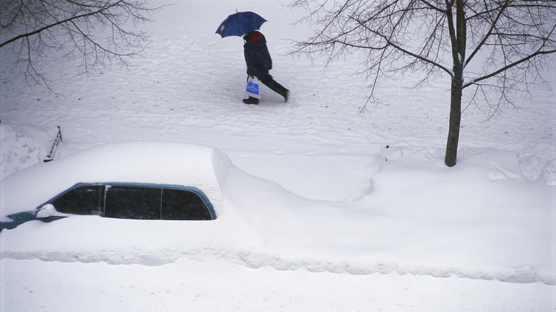 Man walking past car buried in snow from blizzard