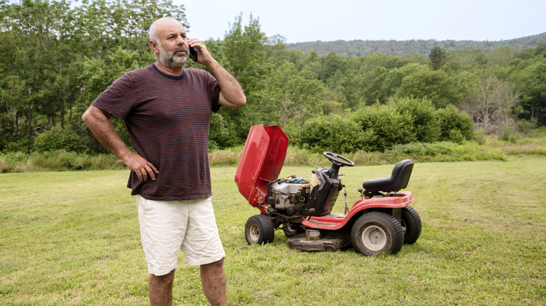 Man on phone next to broken lawn mower