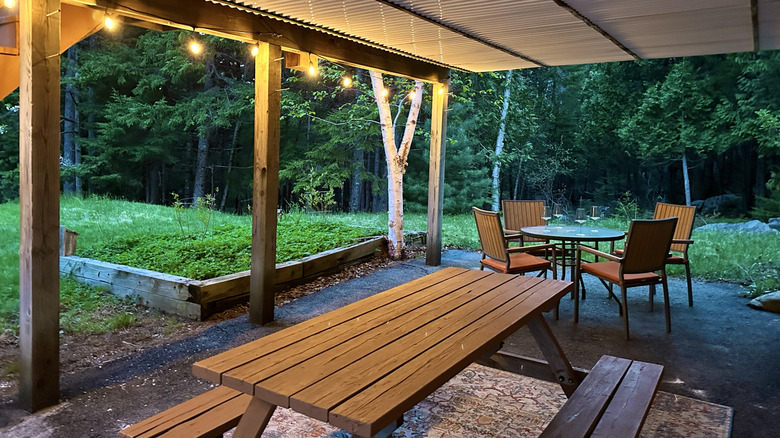 A covered patio at dusk with some hanging lights illuminating the table and chairs.