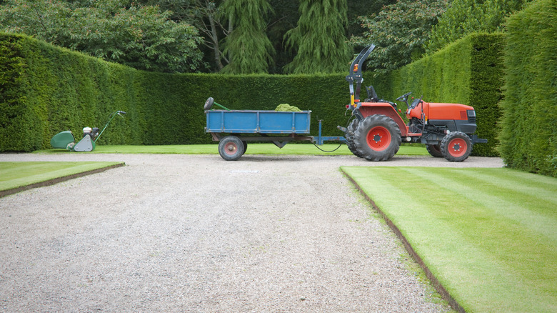 A tractor with a trailer sits on a gravel path in a garden