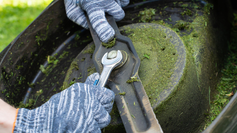 A landscaper adjusting their lawn mower blades with a wrench