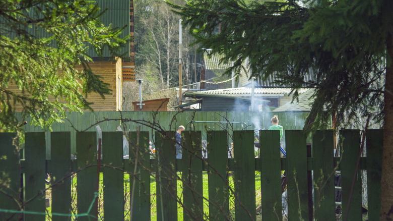 Green fence, with neighbors having bbq outside in background