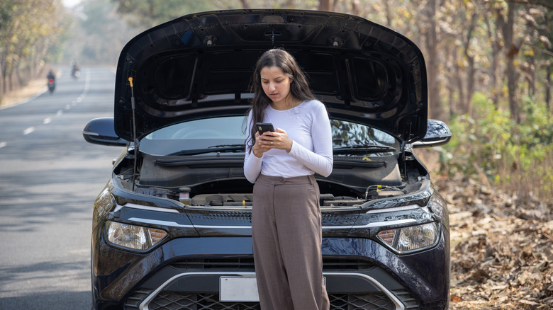 Young woman standing by a broken down car, looking for cell signal
