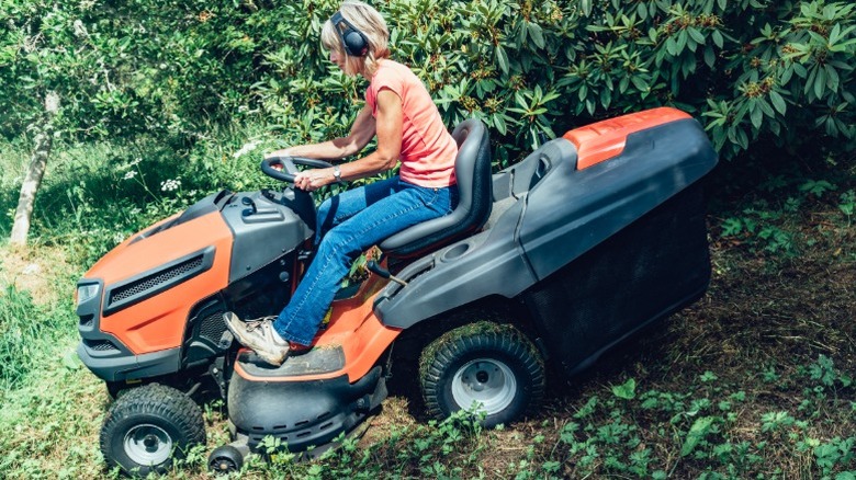 A woman riding a mower down a slight hill