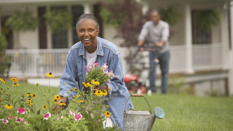 couple works on yard together, woman working on the garden and the man mowing in the background