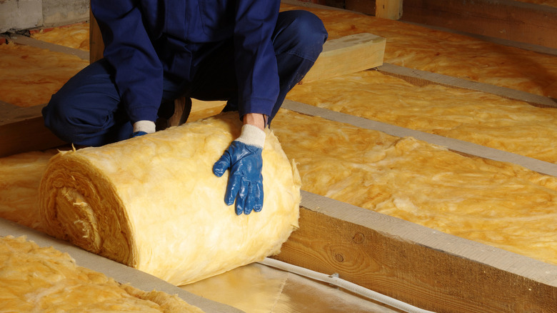 Person unrolling insulation in attic