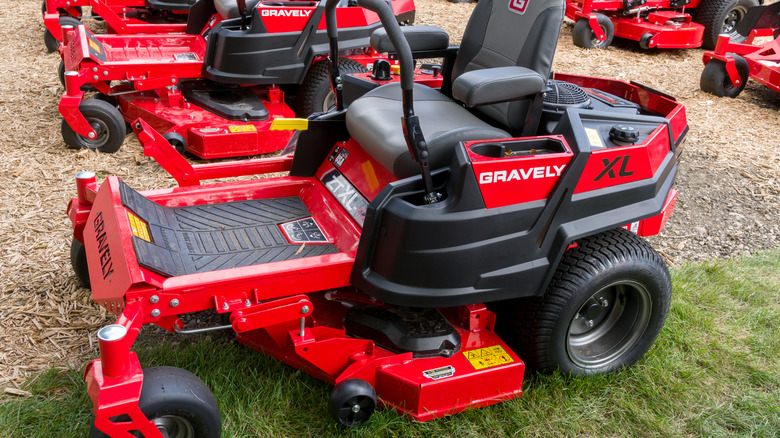 A row of ride-in Gravely lawn mowers sitting outside on grass and mulch