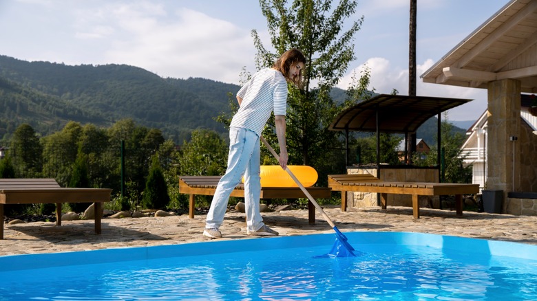 Woman standing on edge of pool and skimming water with net