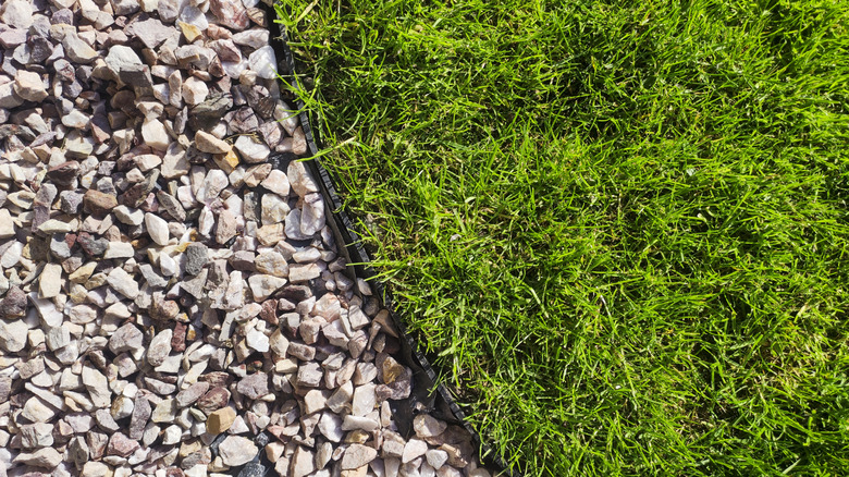 plastic edging along a landscaped rock bed with green grass on one side.