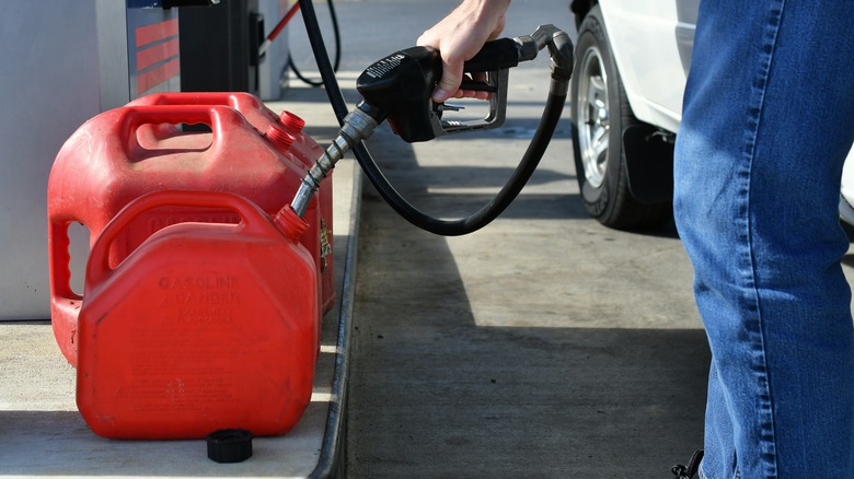 man in jeans fills cans at gas station
