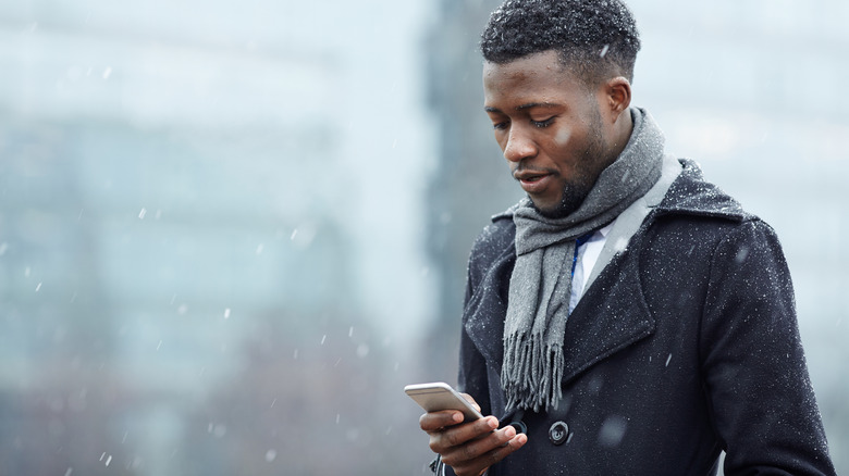 Person checking smart phone in light snow