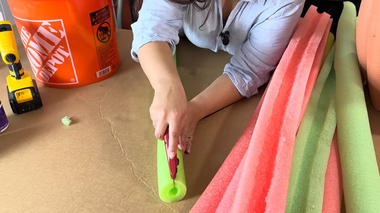Crafter cutting pool noodles in half to make a DIY pumpkin-themed planter for fall.